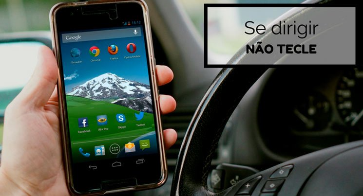 Imagem de uma pessoa segurando o celular dentro do carro com a descrição "Se dirigir, não tecle"